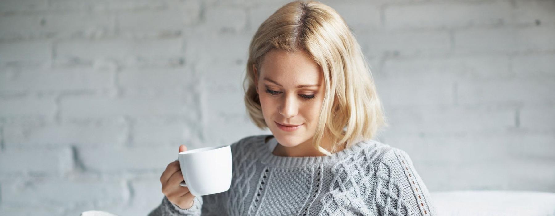 a woman sits on a couch with a cup of coffee and looks at her tablet